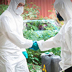 2 individuals in full protective gear shaking hands by a container.