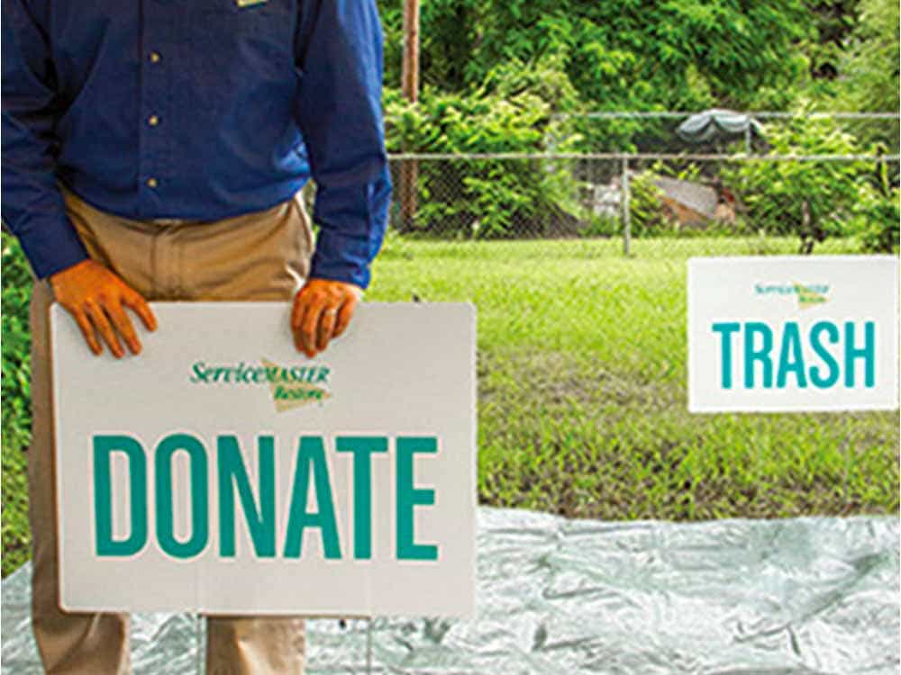 A ServiceMaster expert organizing signs labeled “Donate” and “Trash” in a yard during estate cleanout services