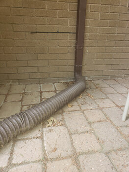A brown flex-drain discharge pipe installed on a gutter downspout