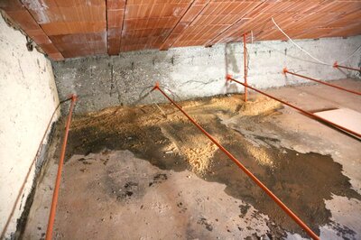 Water damage in a crawl space with a wet concrete floor and exposed subfloor